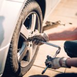 Tire maintenance, damaged car tyre or changing seasonal tires using wrench. Changing a flat car tire on the sideroad